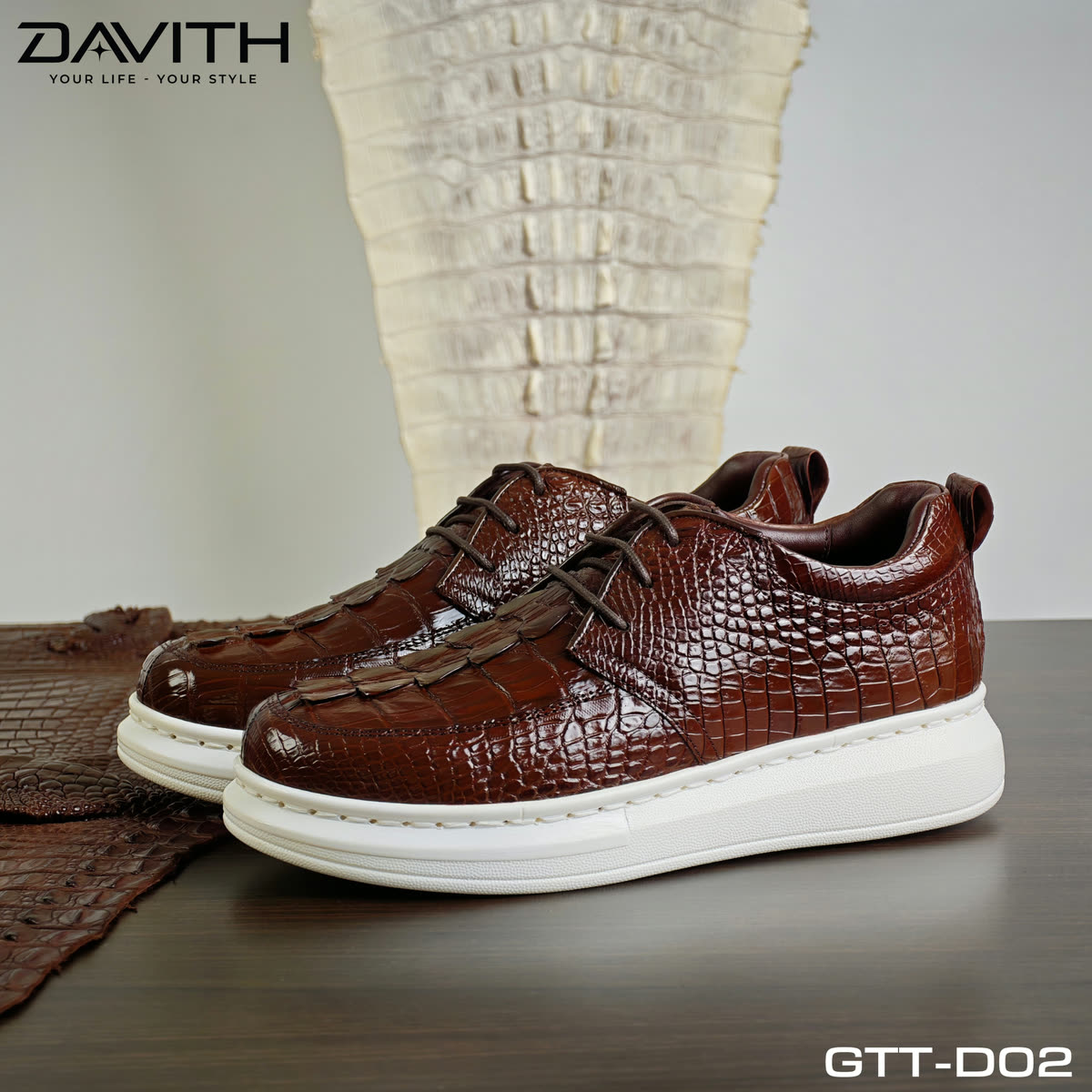 Đôi sneaker GTT-D02 nâu cognac đặt trước tấm da cá sấu
