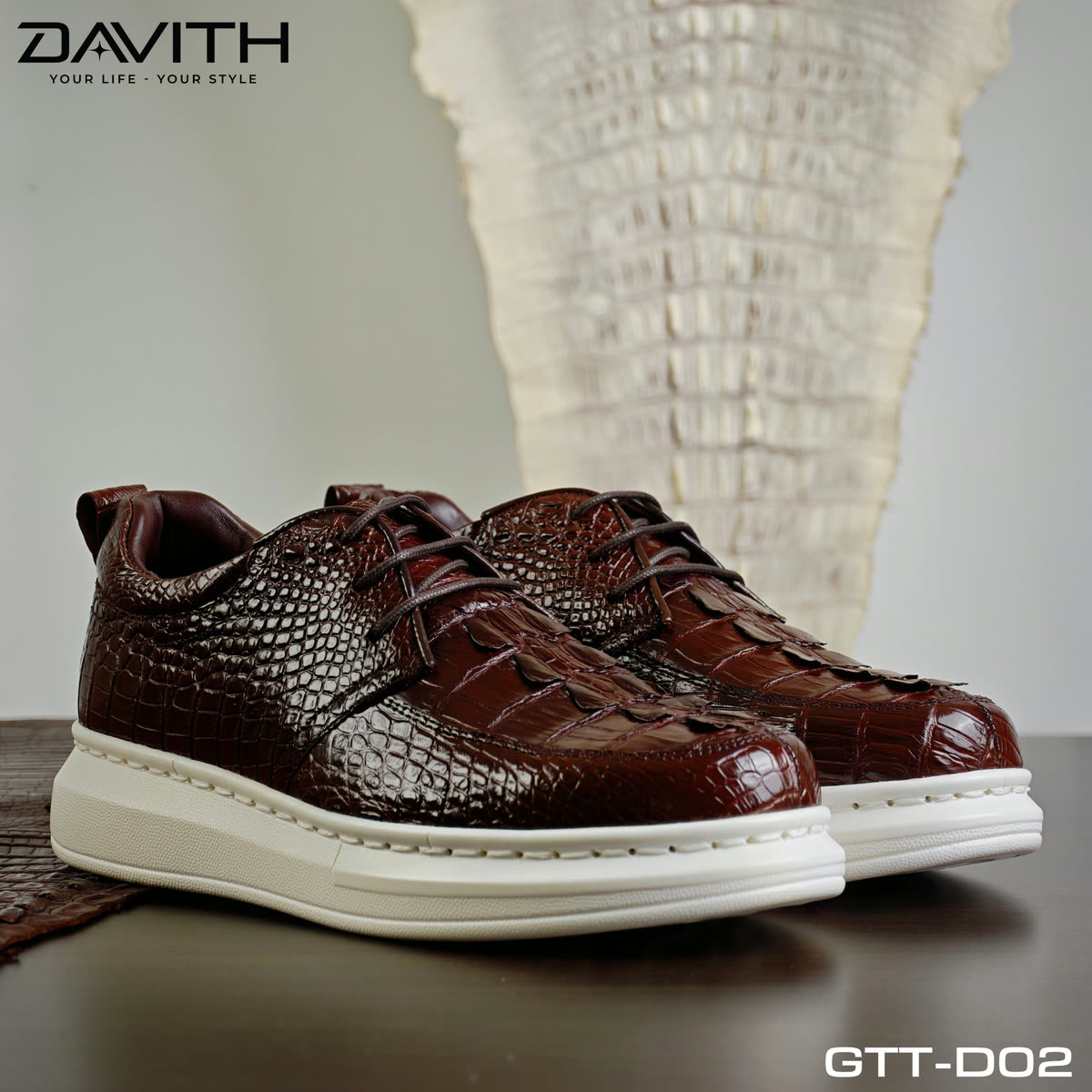 Đôi sneaker GTT-D02 nâu cognac đặt trước tấm da cá sấu