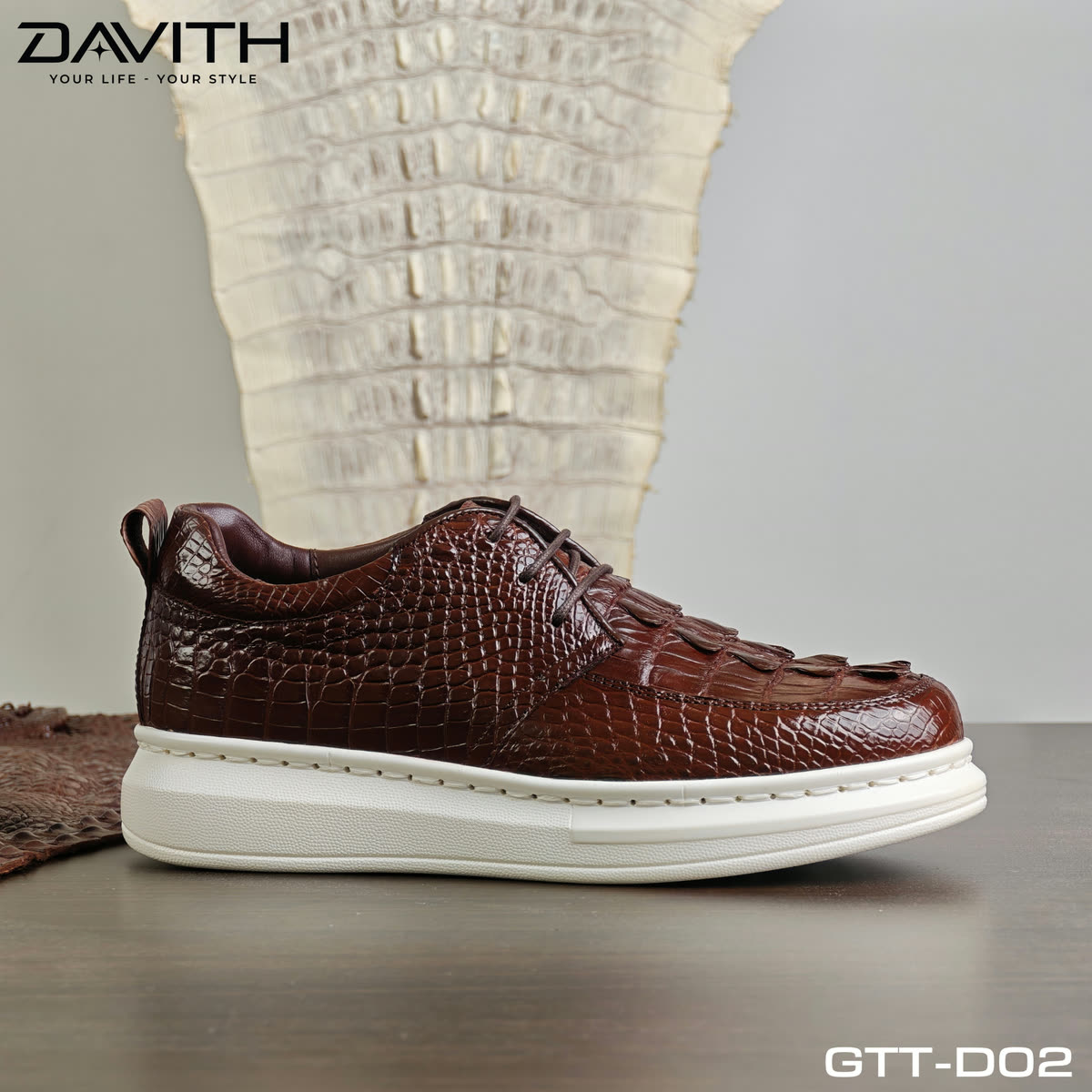 Đôi sneaker GTT-D02 nâu cognac đặt trước tấm da cá sấu